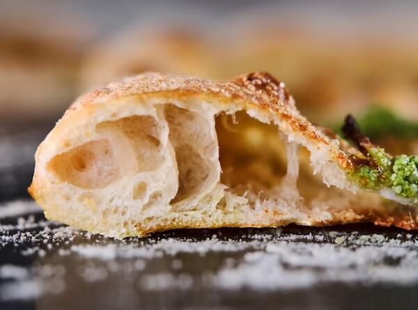 A side profile shot of a open slice of sourdough pizza revealing the characteristic airy pockets inside